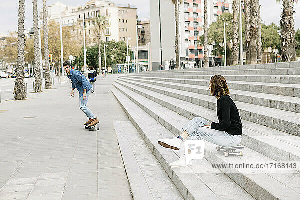 Woman sitting on steps  looking at man skateboarding