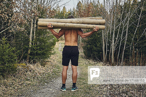 Shirtless male athlete carrying logs in forest