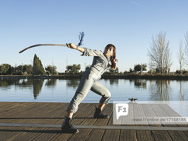 Junge Frau übt Kampfsport mit Schwert gegen See im Park