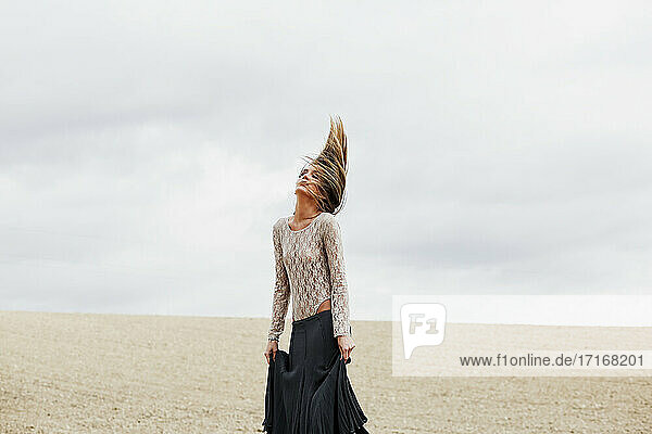 Frau mit Rock  die sich die Haare wirft  während sie am Strand vor dem Himmel steht