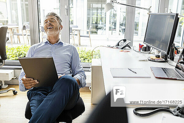 Lächelnder Unternehmer  der ein digitales Tablet benutzt  während er im Büro sitzt