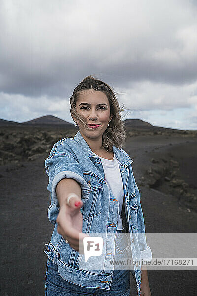Lächelnde Frau  die ihre Hand ausstreckt  während sie auf dem Fußweg am Vulkan El Cuervo steht  Lanzarote  Spanien