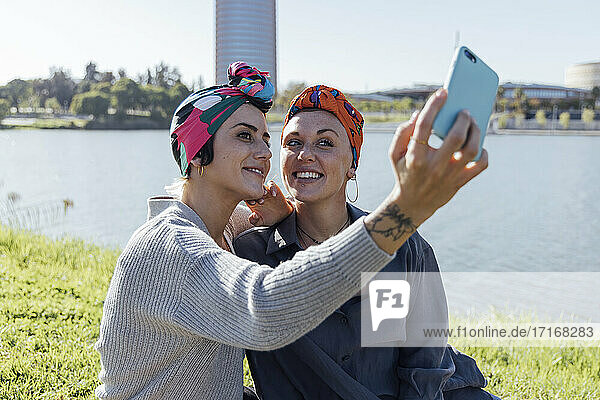 Friends wearing headscarf taking selfie while sitting at park