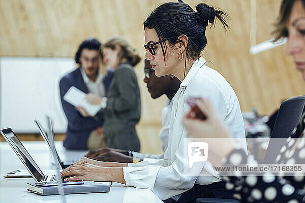 Geschäftsfrau  die einen Laptop benutzt  während sie inmitten von Kollegen in einem Coworking-Büro sitzt