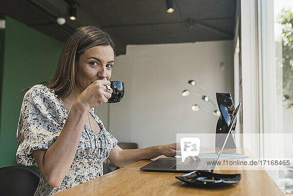 Geschäftsfrau trinkt Kaffee und benutzt einen Laptop auf einem Tisch in einem Café