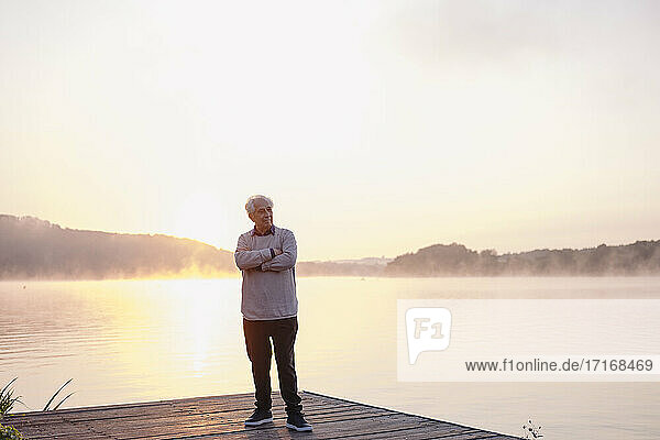 Älterer Mann  der mit verschränkten Armen auf einem Pier steht und wegschaut