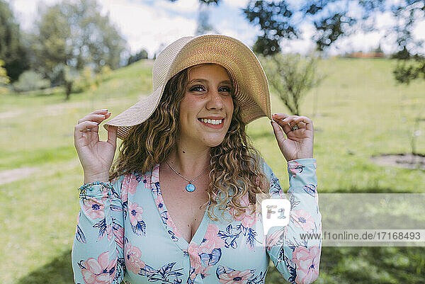 Smiling beautiful woman wearing sun hat in public park during sunny day