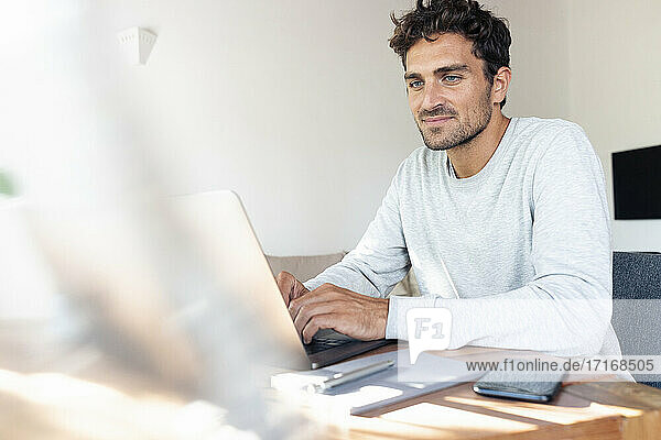 Mittlerer erwachsener Mann  der am Laptop arbeitet  während er zu Hause am Tisch sitzt