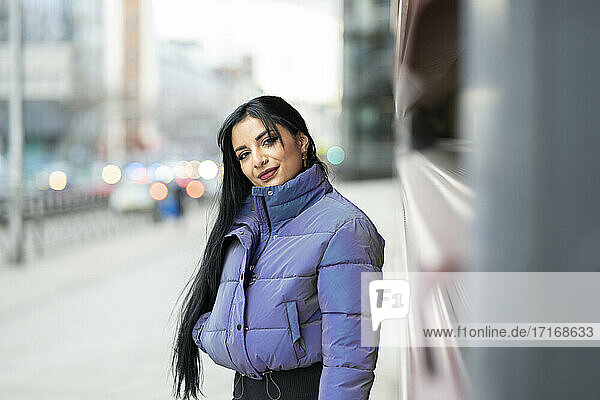 Beautiful young woman in warm clothing standing on street during winter