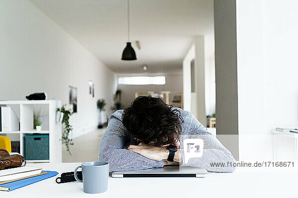 Tired businessman sleeping on laptop in creative office