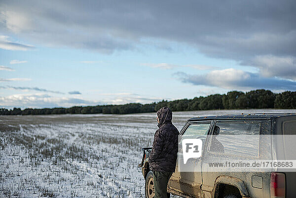 Young man standing by car at agricultural field during winter