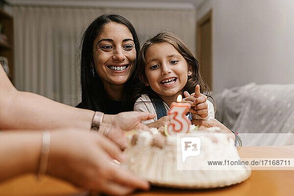 Lächelnde Mutter und Tochter betrachten den Geburtstagskuchen auf dem Tisch zu Hause