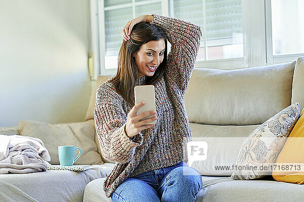 Smiling woman taking selfie on sofa at home