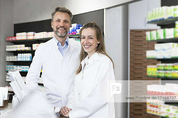 Smiling female pharmacist with male coworker at checkout in store