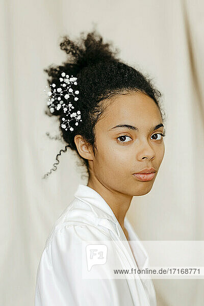 Junge Frau mit weißen Blumen im Haar vor beigem Vorhang