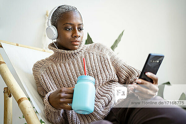 Woman with mason jar using smart phone in living room