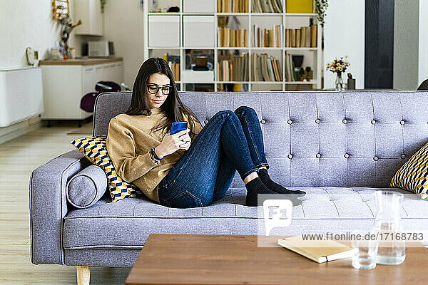 Young woman using mobile phone while sitting resting on sofa at home