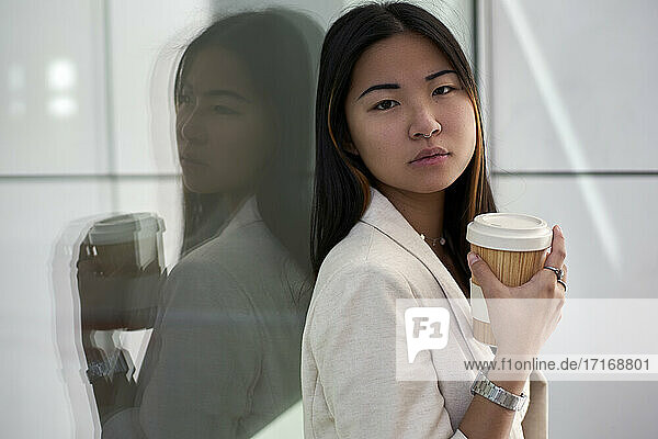 Beautiful woman with reusable cup against glass wall