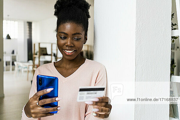 Frau mit Kreditkarte  die lächelt  während sie zu Hause ein Mobiltelefon benutzt