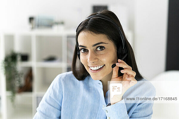 Lächelnde Geschäftsfrau  die ein Headset einstellt  während sie im Büro sitzt
