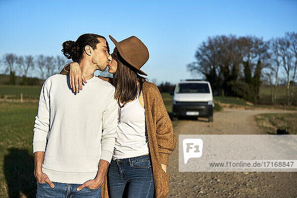 Heterosexual couple kissing while standing against blue sky during sunset