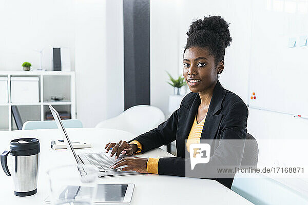 Young Afro businesswoman using laptop while sitting at desk in office