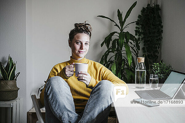 Smiling woman drinking coffee while sitting at home office