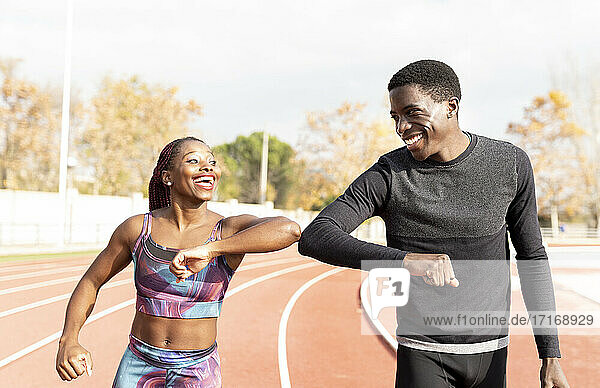 Male and female athlete doing elbow bump while walking on track during sunny day