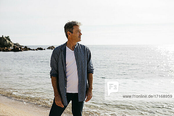 Mature man looking away while standing against sea on beach