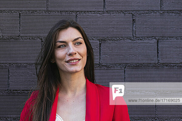 Beautiful smiling businesswoman with gray eyes looking away against brick wall