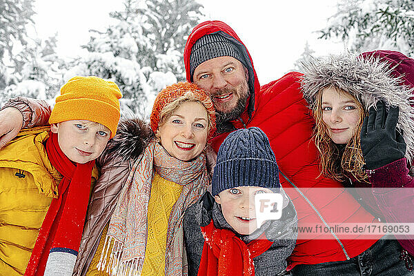 Family smiling while standing with arm around on each other in forest
