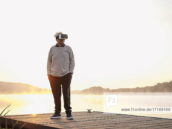 Älterer Mann trägt ein Virtual-Reality-Headset  während er mit den Händen in den Taschen auf einem Pier steht