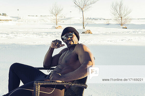 Selbstbewusster Sportler mit Sonnenbrille auf einem Stuhl im Schnee sitzend