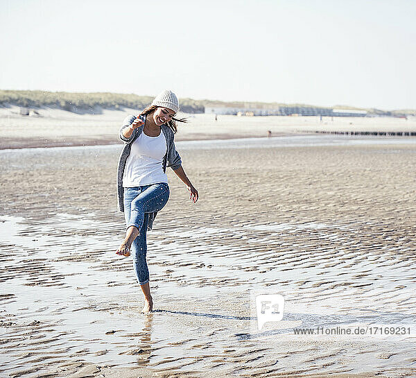 Fröhliche junge Frau  die am Strand spazieren geht und Wasser spritzt