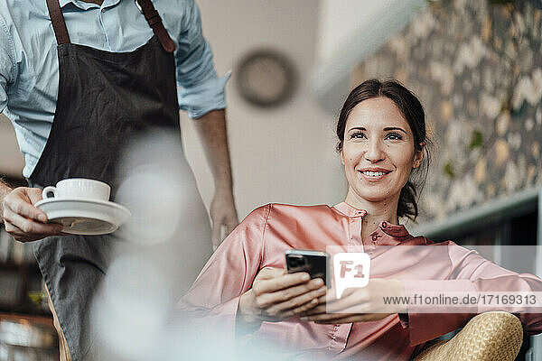 Männlicher Kellner serviert einer lächelnden Geschäftsfrau im Café eine Kaffeetasse