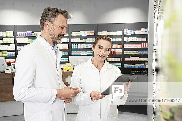Female pharmacist with digital tablet discussing with male colleague