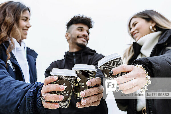 Smiling friend toasting coffee cups while looking at each other