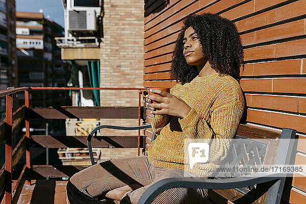 Nachdenkliche Frau mit Kaffeetasse  die wegschaut  während sie auf dem Balkon sitzt