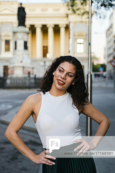 Smiling beautiful woman with arms akimbo standing on street in city