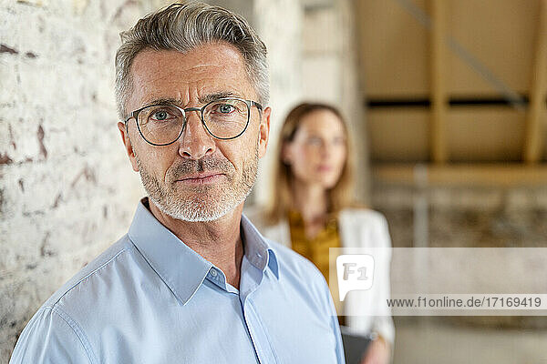 Male engineer staring while standing with colleague in background at construction site