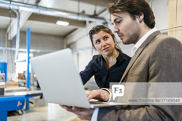 Business people having discussion while working on laptop at industry
