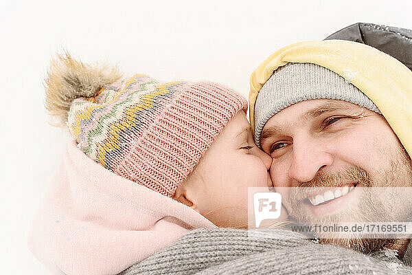 Nahaufnahme einer Tochter  die ihren Vater küsst  während sie im Schnee liegt