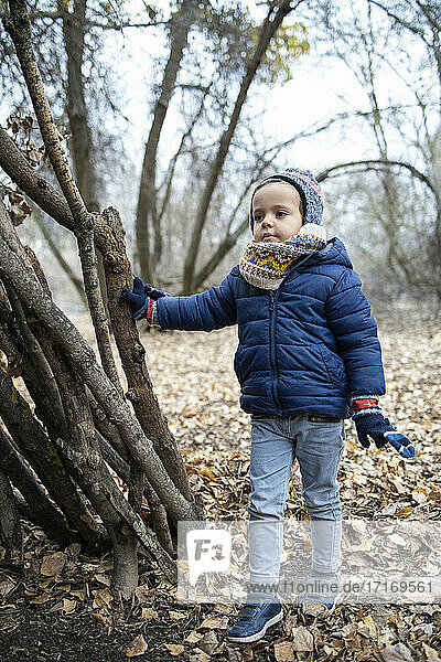 Cute boy wearing warm clothing looking away while standing in forest during autumn