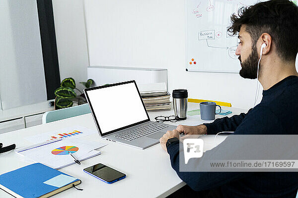 Junger Geschäftsmann schaut auf Laptop in kreativem Büro