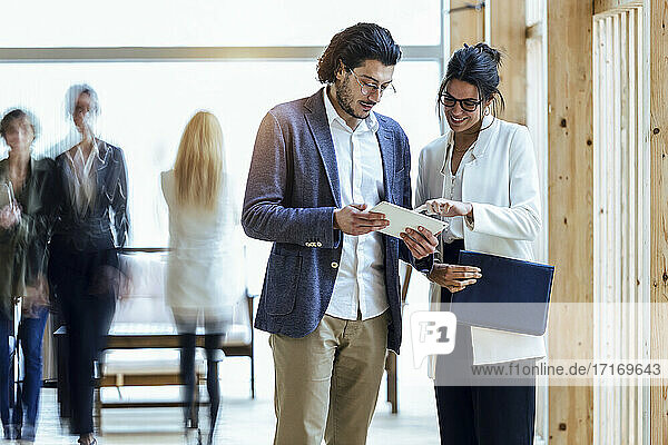 Businessman and businesswoman discussing over digital tablet while standing in corridor at coworking office