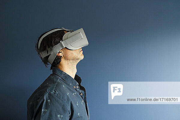 Man watching movie through virtual reality simulator by blue wall at home