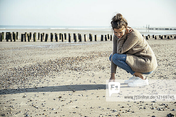Junge Frau in hockender Position auf Sand am Strand