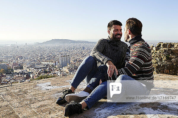 Happy gay couple sitting on observation point during weekend  Bunkers del Carmel  Barcelona  Spain