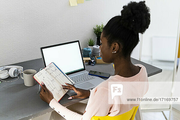 Junge Modedesignerin analysiert Diagramm in Buch bei der Arbeit im Büro zu Hause