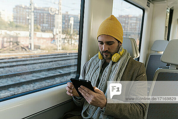 Mittlerer erwachsener Mann in warmer Kleidung  der im Zug sitzend ein digitales Tablet benutzt
